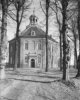 Kerk in achtkantige centraalbouw met tentdak, open lantaarn op het dak, toegangsdeur in omlijsting, rondboognissen in de gevel, pad met bomen op de voorgrond