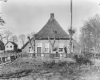 Voorgevel van rietgedekte boerderij, leibomen en tuin op de voorgrond