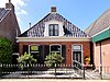 Pand zonder verdieping tegen gevels met houten gootlijst onder hoog schilddak met dakkapellen en topschoorstenen