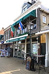 Tot winkel verbouwd pand met verdieping en forse kroonlijst onder zadeldak met voorschild waarboven topschoorsteen