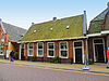Twee woningen onder dwars zadeldak tussen topgevels met beitelingen met gemeenschappelijke schoorsteen met bord