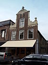 Pand met zadeldak tegen halsgevel met gebeeldhouwde klauwstukken en bekroning in de Friese Lodewijk XIV-stijl