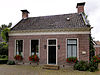 Dwarshuisboerderij met voorhuis tussen twee topgevels met geblokte kroonlijst onder zadeldak met schoorstenen met borden