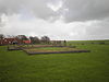 Stryper Kerkhof op Terschelling -01 -  Elevated terrain of former churchyard with restored floor plans of medieval churches, gravestones and sidewalk marking poles.Nationally listed heritage.  Verhoogd terrein voormalig kerkhof met gerestaureerde kerk-plattegronden uit de Middeleeuwen, grafstenen en stoepstenen.