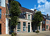 Groot dorpshuis met omlijste ingang en zesruitsvensters onder twee evenwijdige zadeldaken tussen topgevels met hoekschoorstenen