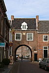 Buren - Voorstraat - Huizerpoort.JPG -  Van de poorten resteert de Culemborgse- of Huizerpoort. De overwelfde rondboogdoorgang is laat-14de-eeuws. De verdieping met zadeldak tussen twee topgevels is in de 17de eeuw vernieuwd. De gevel aan de stadszijde en de bogen zijn in 1816 nieuw opgetrokken. De zonnewijzer aan de stadszijde dateert uit 1631. 