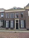Pand met eenvoudige lijstgevel waarin deurpartij met jonische pilasters, schuiframen uit de bouwtijd en kroonlijst met triglyphen en metopen