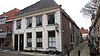 Hoekpand met hoog, gewijzigd schilddak en gepleisterde lijstgevel. Keistoep met hekpaal