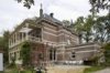 Zicht op de achter- en de rechterzijde, met houten serre en bovengelegen veranda, rechts de annex