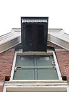 Te Kortschot detailfoto pakhuis -  Detail van het opgeklampt dubbele laadluik, met daarboven een houten takelomkapping bestaande uit een vertikale beschieting voorzien van een decoratief gezaagde rand