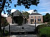 Boerderij Den Hoek te gameren -  Het VOORHUIS van deze boerderij is gebouwd op een nagenoeg vierkant grondplan en telt twee bouwlagen - waarvan de tweede bouwlaag niet een volledige verdiepingshoogte heeft - en een zolder. Het afgeknotte tentdak is gedekt met gesmoorde oudhollandse pannen. Drie gemetselde schoorstenen staan op de nok. De gevels zijn opgetrokken in baksteen. Het metselwerk is uitgevoerd in kruisverband. Langs voor- en zijgevels loopt een gepleisterde plint. De verdiepingen worden gemarkeerd door een rondomlope…