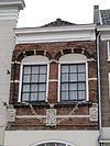 Pand met gevel, waarvan de trapgevelbekroning vervangen is door een rechte kroonlijst. Boven de pui twee leeuwenmaskerconsoles en een gebeeldhouwde gevelsteen, voorstellend het offer van Abraham. Hierboven een geprofileerde, bakstenen waterlijst met maskerkopje.