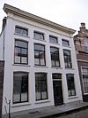 Pand, bestaande uit twee huizen onder schilddaken, in het derde kwart 19e eeuw samengetrokken achter een gepleisterde lijstgevel ter breedte van vier vensterassen