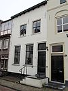 Korte Steigerstraat 15 - Pand met verdieping en zadeldak, evenwijdig aan de straat. Het waarschijnlijk 17e eeuwse pand wordt aan de zuidzijde afgesloten door een puntgevel. De gepleisterde voorgevel heeft in de verdieping vierruits Empireschuiframen met gegroefde middenstijlen 
