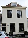 Ruiterstraat 29 - Pand met verdieping en schilddak. Gepleisterde gevel onder 19e eeuwse kroonlijst. Gesneden deur uit begin 19e eeuw met gestoken kalf. Bovenvensters met zesruitsschuiframen. 