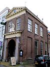 Oliestraat 1 - De Waag. Smal, rechthoekig bakstenen gebouw met verdieping en schilddak, ontworpen door C. van Leeuwen en gebouwd van 1796 tot 1798. De voorgevel aan de Markt heeft een getoogde inrijpoort, geflankeerd door twee hardstenen, Dorische pilasters, die een hoofdgestel dragen, waarboven een gesneden Justitiabeeld. Het vertrek boven de Waagruimte heeft twee vensters, waarin sinds een recente restauratie 15-ruitsschuiframen. De gevel wordt bekroond door een houten kroonlijst met in het fries triglyphen…