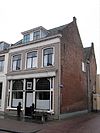 Pand op de hoek van de Zandstraat, bestaande uit twee parallel lopende vleugels, elk onder een zadeldak tussen puntgevels met vlechtingen. In de zijgevel van de achterste vleugel aan de Zandstraat togen van dichtgezette vensters en zeven sierankers