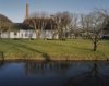 Linker zijgevel en schoorsteen voormalige oliemolen met water op de voorgrond (Damsterdiep)