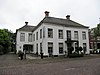 Bellingwolde Hoofdweg 162 - Pand bestaande uit twee blokvormige gedeelten, ieder gedekt door een laag schilddak met hoekschoorstenen waarop borden; omgaande gootlijst. Oorspronkelijk als raadhuis en cafe in gebruik geweest.