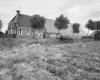 Overzicht voor- en zijgevel boerderij met bomen op de voorgrond