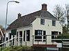 Schouwerzijl - zijlhuis -  Voormalig zijlhuis van Schouwerzijl naast de vroegere Schouwerzijl in de Kromme Raken. Gebouwd in 1851 op de plek van een oudere gelijksoortige woning, twee jaar nadat de houten sluis was vervangen door een stenen sluis. Op de rechter schoorsteen prijkt een witkleurige gek (slecht zichtbaar) in de vorm van een aal. Op de muur staat het wapen van het waterschap Hunsingo (combinatie van wapen van Winsum en van het Winsumer en Schaphalsterzijlvest).