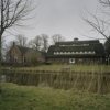 Overzicht van de bijgebouwen, links het woongedeelte en rechts het bedrijfsgedeelte, gracht op de voorgrond