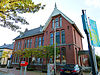 Zuidhorn - postkantoor - rechts -  Voormalig postkantoor met ingebouwde dienstwoning aan de Hoofdstraat 30 van Zuidhorn. Gebouwd tussen 1907 en 1908 door aannemer J. Wolrick uit Hoogezand naar een ontwerp van rijksbouwmeester Cornelis Peters in de zogenoemde 'postkantorengothiek'. In 1978 uitgebreid aan achterzijde (valt buiten bescherming). In de linker zijgevel zijn in 1983 een paar nieuwe vensters geplaatst. In 1990 werd aan voorzijde een invalidenopgang geplaatst en werd het interieur gemoderniseerd. Ergens begin 21e eeuw w…