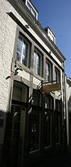 Huis met lijstgevel, voorzien van gekoppelde segmentboogvensters in hardsteen, onderling verbonden door verticale reliefbanden.