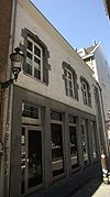 Huis met lijstgevel, geknikt in verband met de ligging in de bocht van de straat. Links een rondbogige koetspoort in Naamse steen.