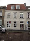 Huis met gebosseerd witgepleisterde lijstgevel en met rode pannen belegd zadeldak
