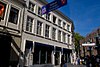 Breed pand met gebosseerd gepleisterde lijstgevel boven geheel doorlopende moderne vitrines