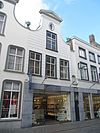 Huis met gebosseerd gepleisterde ingezwenkte halsgevel, gedekt met driehoekig fronton