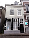 Huis met gepleisterde lijstgevel met dakkapel, schuiframen bovenlicht met elkaar kruisende segmenten