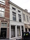 Huis met schilddak en gebosseerd gepleisterde lijstgevel waarin cordonlijsten en schuiframen
