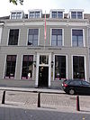 Huis met gebosseerd gepleisterde gevel met kroonlijst op consoles, schuiframen en omlijste ingangspartij