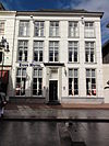 Huis met gebosseerd gepleisterde gevel met schuiframen en ingangspartij bestaande uit geblokte pilasters met kroonlijst waaronder triglyphen met druppen