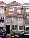 Huis met schilddak en lijstgevel, met op de verdieping mozaiekversiering in baksteen, bestaande uit sterren; korfbogige ontlastingsbogen met natuursteenblokken, ankers. Winkelpui