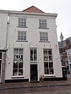Groot huis op de hoek van de Markt, met hoog schilddak en gebosseerd witgepleisterde lijstgevels, bovenramen met kleine witte roedenverdeling; tegen de zijgevel drie steunberen. Beganegronds verbouwd