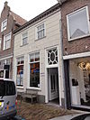 Huis met gebosseerd witgepleisterde lijstgevel, kroonlijst op klossen en schilddak