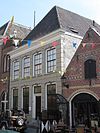 Huis met hoog schilddak en gebosseerd grijsgepleisterde lijstgevel, waarin vensters met afgeronde bovenhoeken en stuckuiven