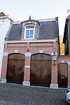 Heusden - Hoogstraat 18 - Koetshuis - Pakhuis.JPG -  Koetshuis / Pakhuis, omstreeks 1895 opgetrokken in Eclectische- en Neo-renaissancestijl. Het koetshuis bevindt zich twee huizen ten zuidwesten van nummer 24 (onderdeel II van dit complex). Aan de rechterzijde is een bijbehorend klein inrijpoortje gelegen. 