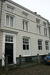 Heusden - Stadshaven 22 - Woonhuis.JPG -  Huis met gebosseerd grijsgepleisterde lijstgevel en met witte deuromlijsting. 