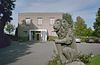 Stenen tuinornament (leeuw met wapen) met bijgebouw op de achtergrond - Nieuwkuijk - 20333287 - RCE -  Abdij Marienkroon: Stenen tuinornament (leeuw met wapen) met bijgebouw op de achtergrond 