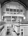Interieur van de synagoge te Tilburg, gezien vanaf de oostzijde naar de vrouwengalerij, met biema (= verhoging voor het voorlezen van de Tora) en kroonluchter - Tilburg - 20209524 - RCE -  Synagoge: Interieur van de synagoge te Tilburg, gezien vanaf de oostzijde naar de vrouwengalerij, met biema (= verhoging voor het voorlezen van de Tora) en kroonluchter 
