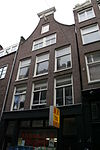 Uitwendig voornamelijk 19e-eeuws huis waarvan de gevel wordt bekroond door een klokvormige top onder rollagen en afsluitende lijst