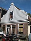 Houten dijkhuis met klokgevel (uit- en ingezwenkt voorschot) uit 19de eeuw, bakstenen onderpui