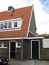 Blok met 8 keukenwoningen, zo genoemd vanwege destijds nieuwe plaatsing van keuken aan de voorzijde, aan de zijkant een houten topgevel, bouwstijl Amsterdamse School, samen met de poortgebouw langs de Purmerweg centraal deel van Tuindorp Nieuwendam