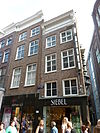 Hoekhuis met voorgevel onder rijk gesneden rechte lijst met consoles. Opmerkelijke zijgevel uit de bouwtijd, ten dele overgebouwd op gesneden puibalk en dito balkkoppen; tweelichten