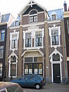 WLM - Minke Wagenaar - 126 2658 - Omschrijving rijksmonument Bakstenen remisedeel met de voorgevel aan de Schinkelhavenstraat 27 en de achtergevel aan de Eerste Schinkelhavenstraat 16. Aan de oostzijde grenst het gebouw aan het binnenterrein. De voorgevel geeft de onderverdeling van dit deel van het gebouw in drie bouwlagen weer: hoofdverdieping, verdieping en kapverdieping. Op de hoofdverdieping een brede toegangsdeur met luifel. Onder de overkapping van de luifel de initialen van de A.O.M. tussen florale decoratie. Ter rechte…