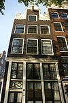 Hoekhuis met boven de houten pui in 18e-eeuwse stijl herbouwde gevel waarop hals met gedeelte vleugelstukken, vazen op de krullen en een schelp in de afdekking